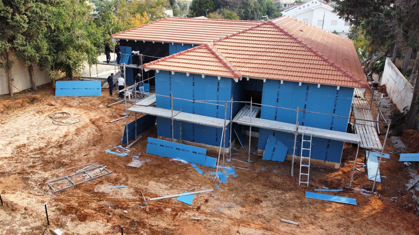 בית בבנייה עם גג רעפים כתום ויריעות כחולות על הקירות